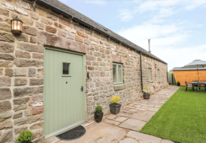 A traditional honey-colored Cotswold stone cottage exterior with climbing roses, nestled in the picturesque village of Churchill.